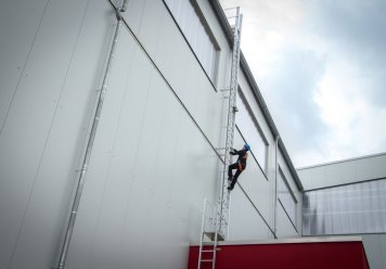 pracovník, ktorý lezie po rebríku na bočnej strane budovy